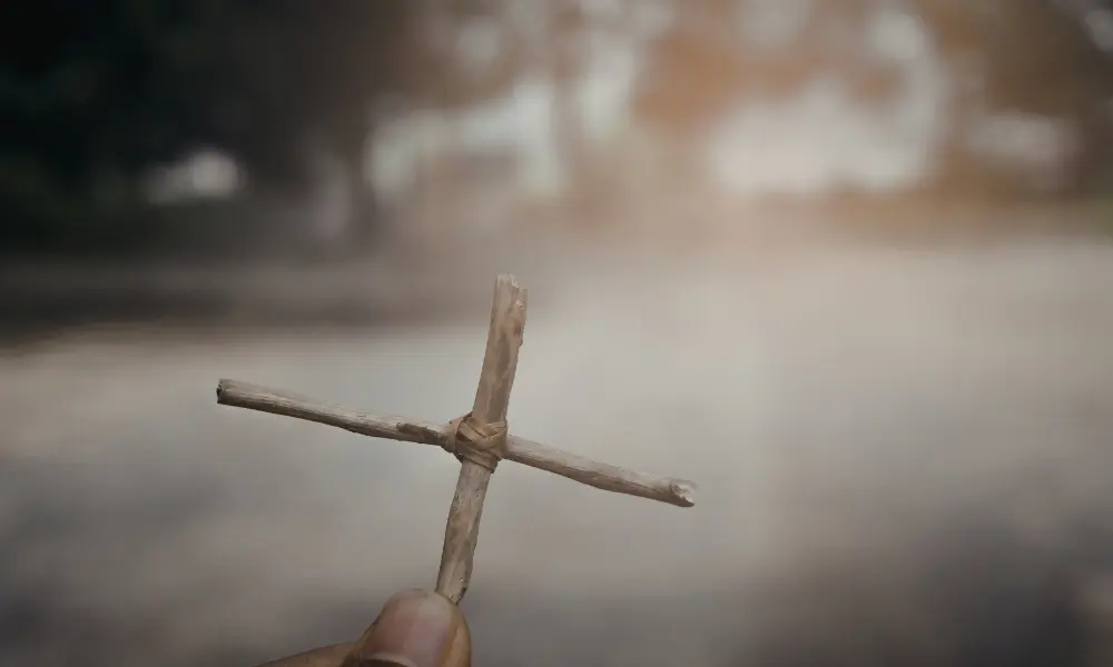 a finger holding a cross made from branches