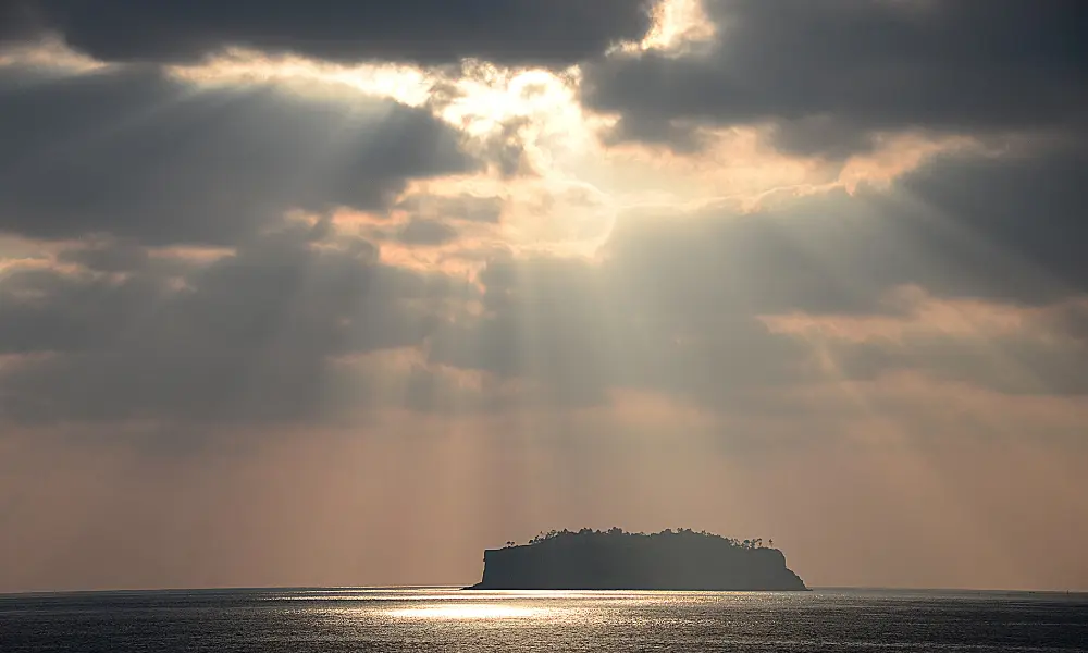 烏雲散開有好幾道光照下來到一個海面的島嶼上